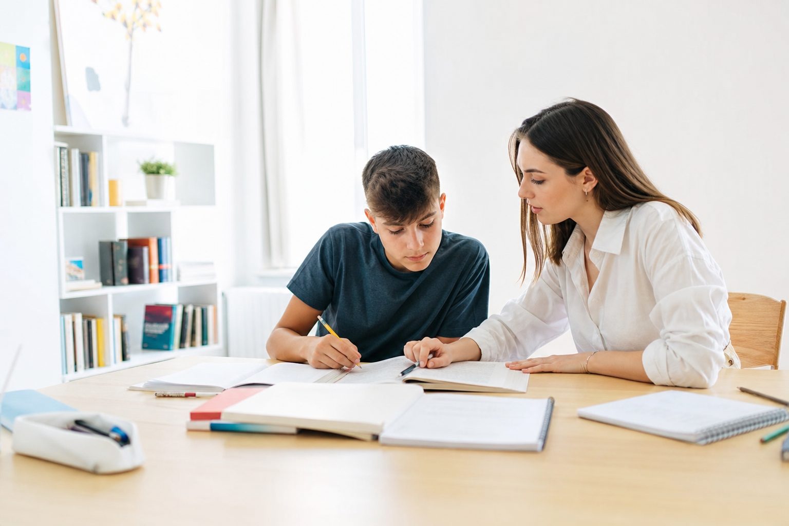 Una tutor segue un ragazzo delle superiori al tavolo di studio, tra quaderni e libri aperti.
